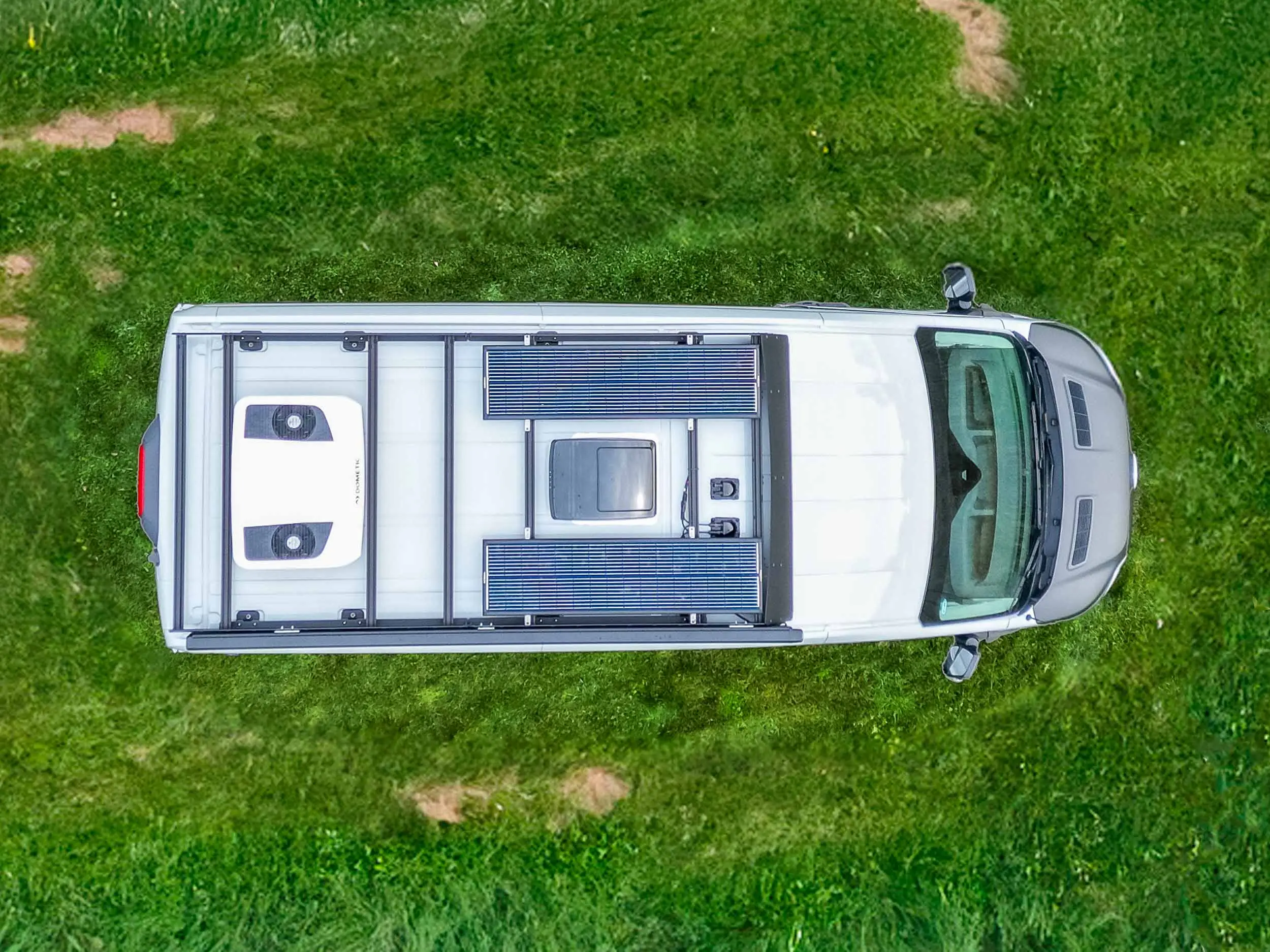 Straight-down aerial view of the current Link 148 roof: two solar panels flanking the vent fan and skylight, the rooftop air conditioner, and the flatline roof rack